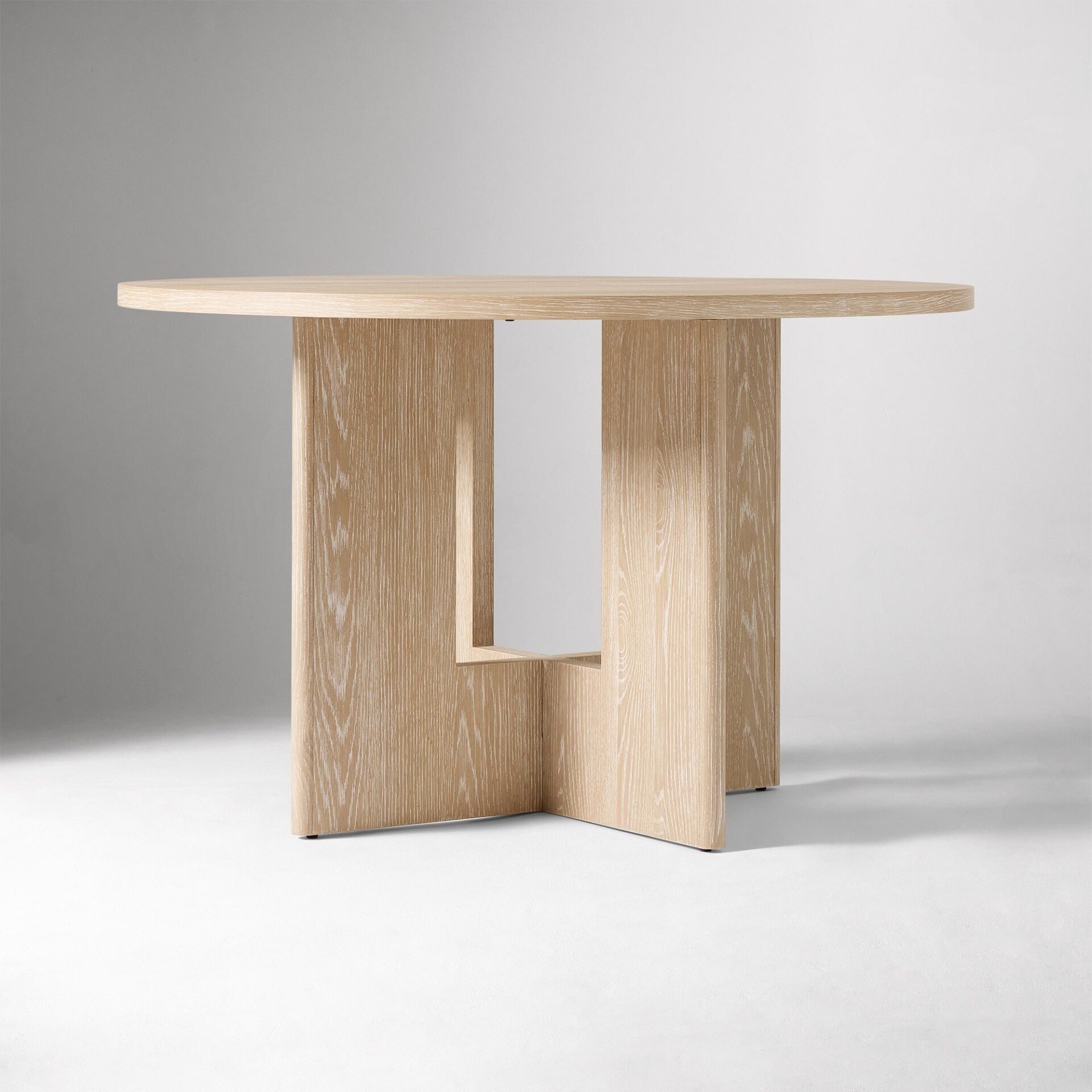 ELVANO solid teak round dining table handcrafted in Jepara with architectural cut-out panel legs.